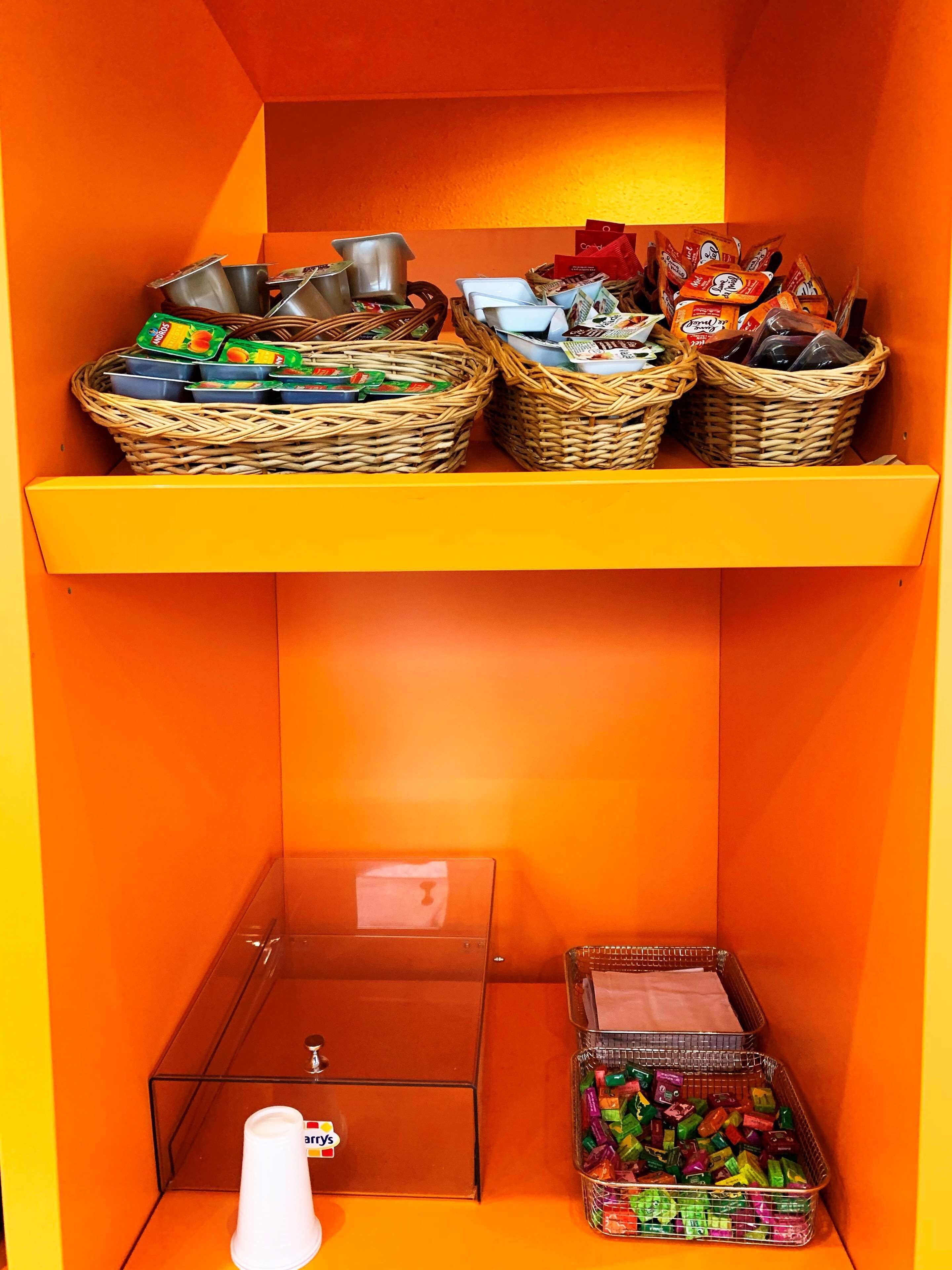 A small storage area with wicker baskets containing snacks and drinks, a clear plastic box, and a small white container.