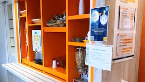 Ein Empfangsbereich mit Theke, einer Selbstbedienungsgetränkeausgabe und Informationsplakaten an der Wand.