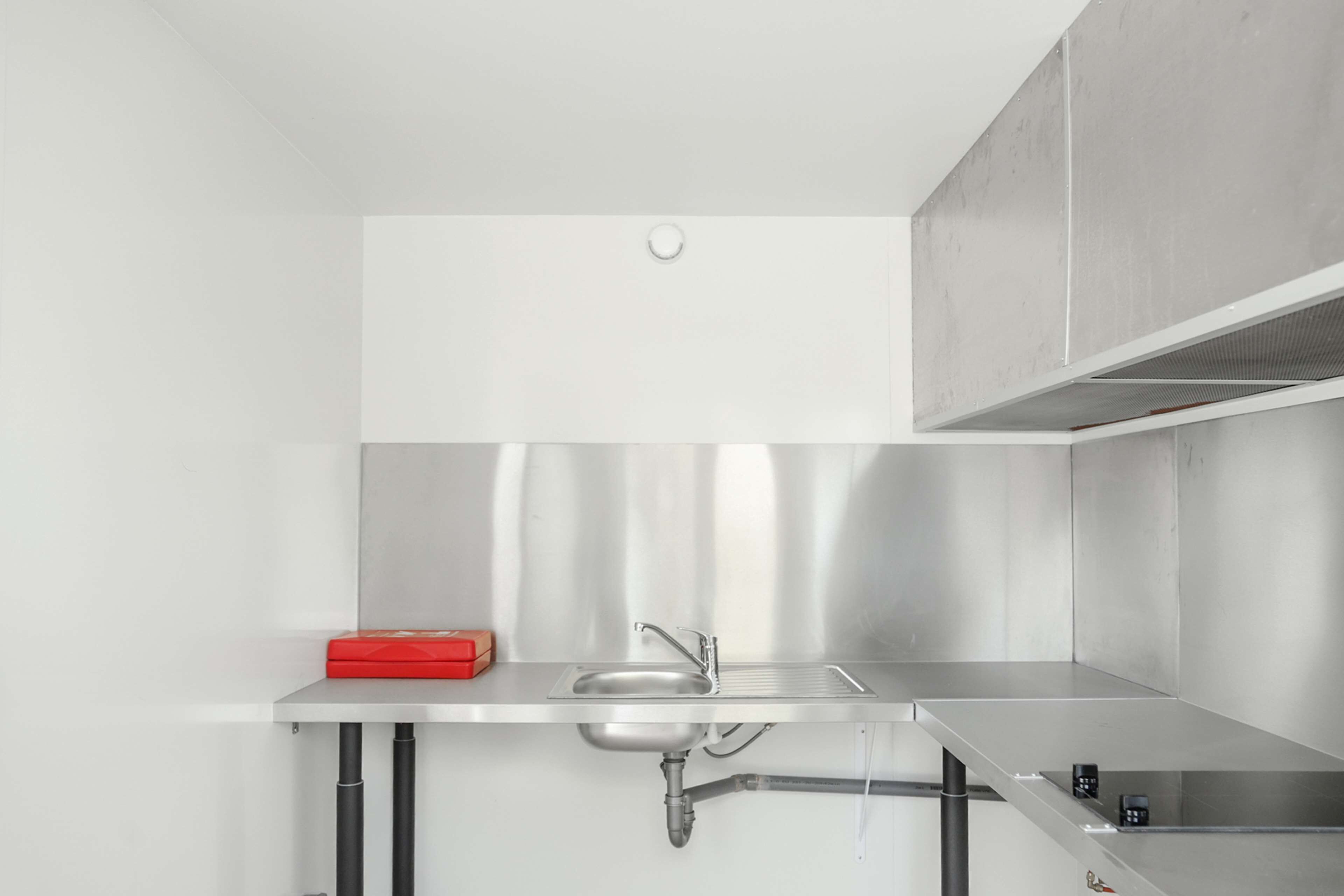 A modern kitchen with a stainless steel sink, a red box on the counter, and a ventilation hood above.