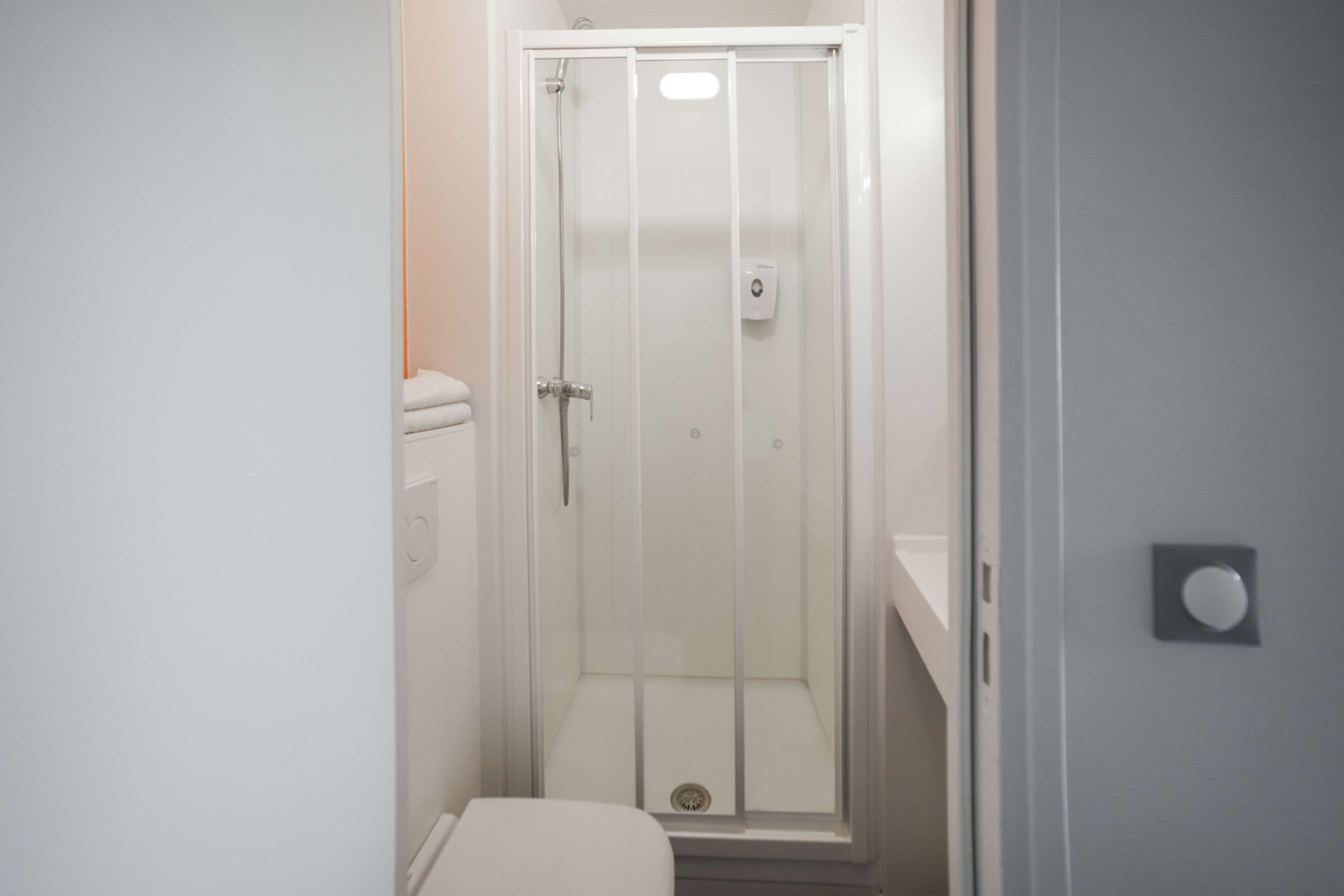 A small, enclosed shower area with a glass door, a toilet, and a wall-mounted light fixture.