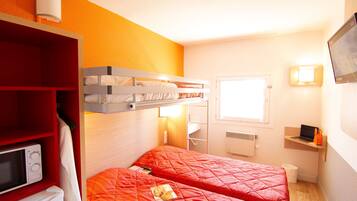 A room with two beds, a red wardrobe, a microwave, a small desk with a laptop, and a window.
