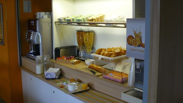 Ein Frühstücksbereich mit einer Kaffeemaschine, einem Toaster und verschiedenen Speisen wie Brot und Gebäck.