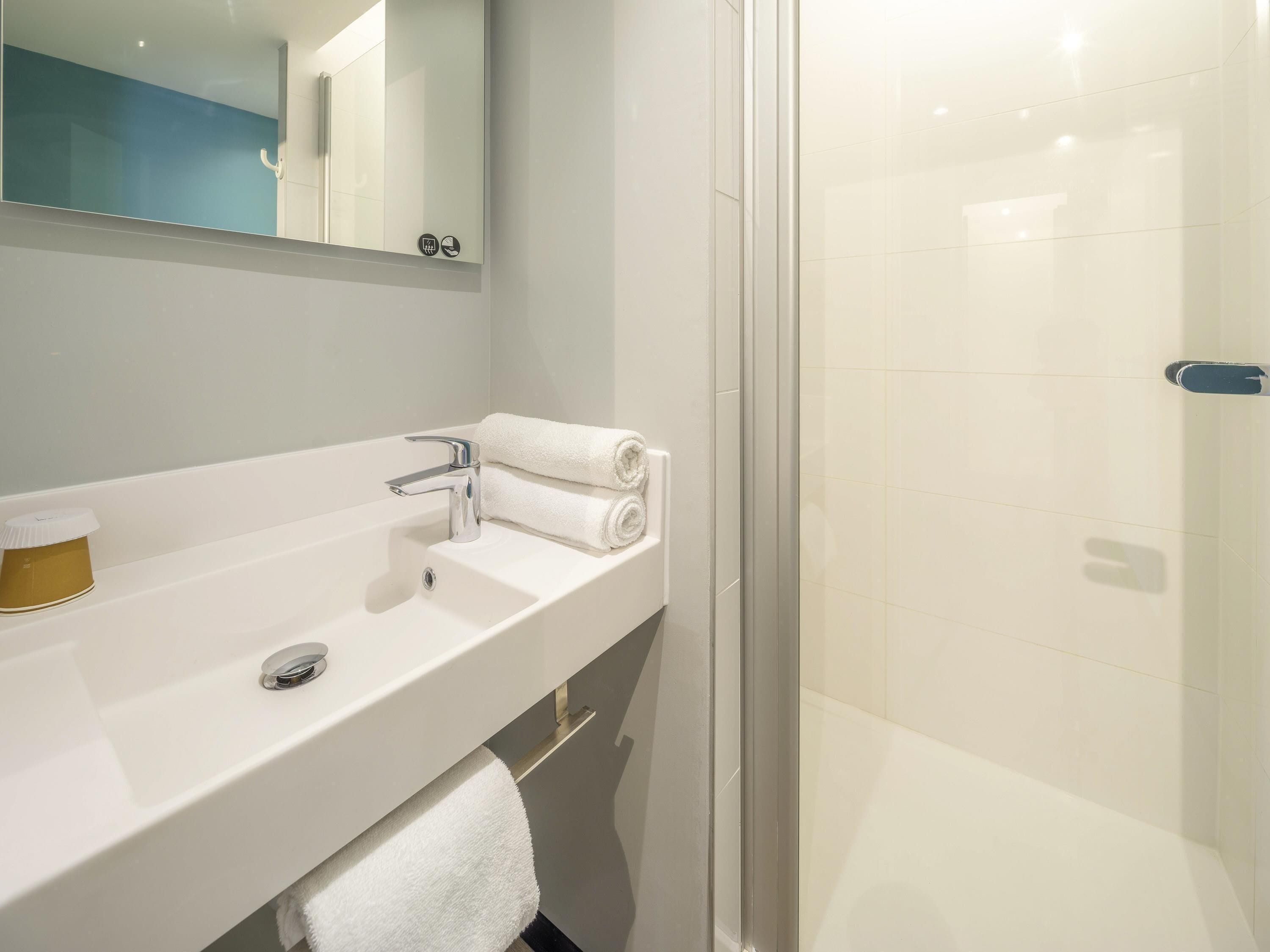 A bathroom with a white sink, a mirror, a towel, and a shower area.