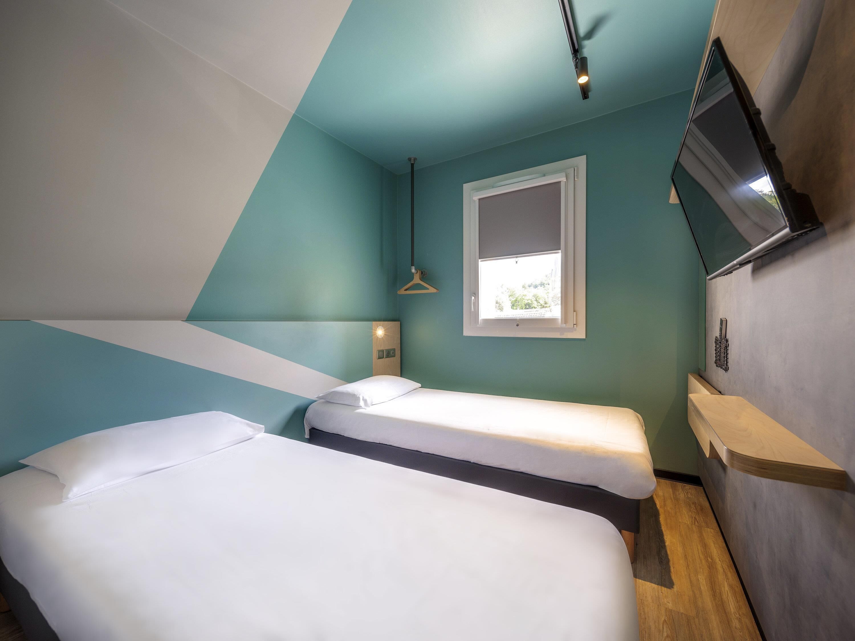 Un dormitorio moderno con dos camas, una ventana, un televisor y una lámpara colgante.