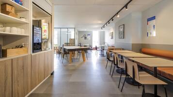 A spacious indoor area with multiple tables and chairs, a coffee machine, and shelves with various items.