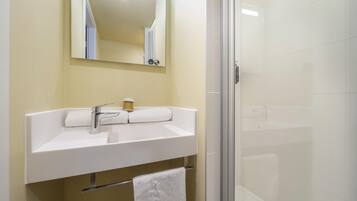 Une salle de bain avec un lavabo blanc, un miroir et une cabine de douche en verre.