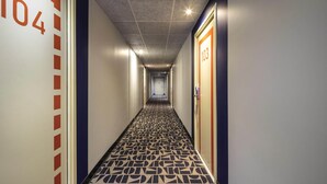 A hotel hallway with a patterned floor, numbered doors, and a textured ceiling. - ibis budget Forbach Centre (Forbach)