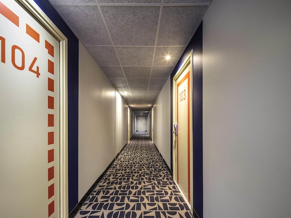 A hotel hallway with a patterned floor, numbered doors, and a textured ceiling.