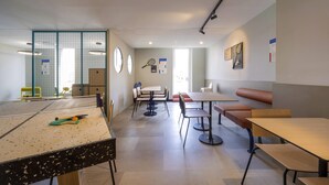 A modern indoor space with a ping pong table, seating areas, and a sports wall. - ibis budget Forbach Centre (Forbach)