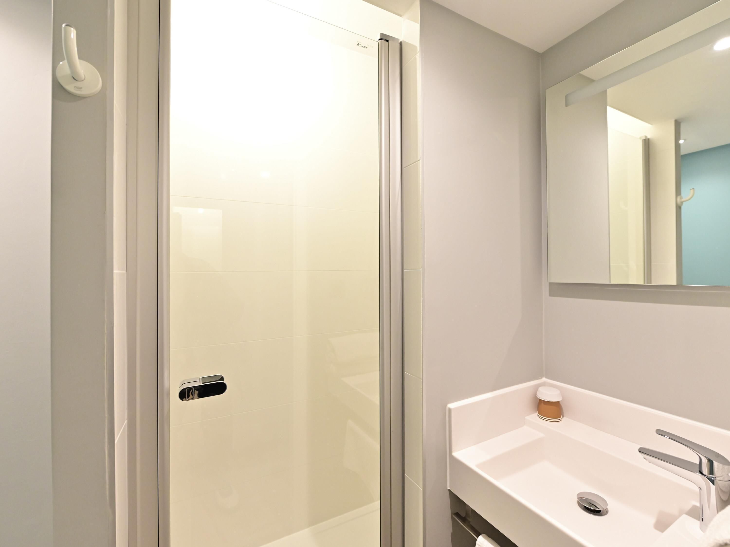 Un baño moderno con mampara de vidrio, un lavamanos blanco con grifo cromado y un espejo sobre el lavamanos.