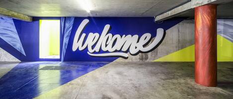 An underground parking garage with a 'Welcome' sign, concrete pillars, and a sloped ceiling.