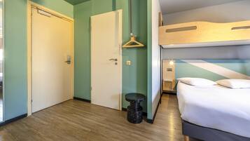 Hotellihuone, jossa on kerrossänky, pieni pyöreä jakkara ja riippuvalaisin.