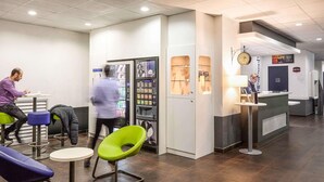 Un hall d’entrée moderne avec des espaces de détente, un distributeur automatique, un comptoir d’accueil et une horloge murale.