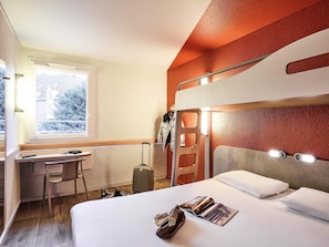 A bunk bed room with a desk, suitcase, and a window with a view of trees.