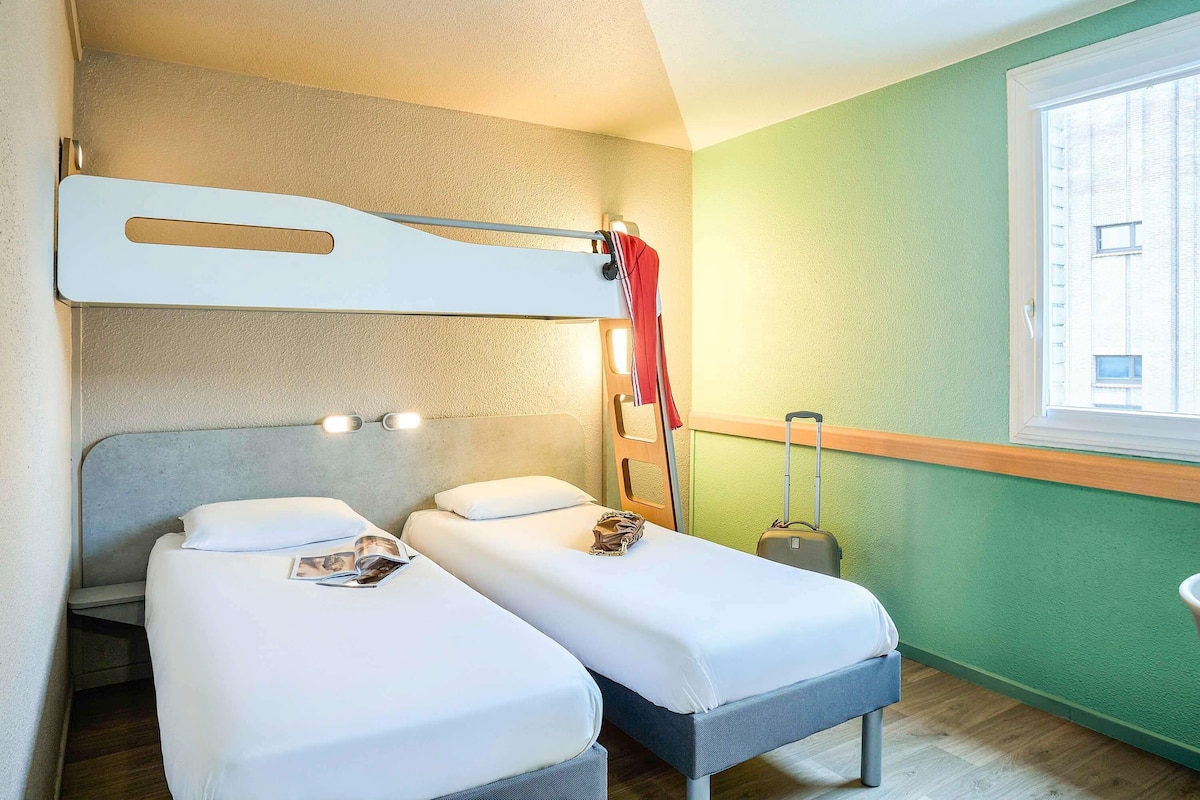 A room with bunk beds, a suitcase, a window with a view, and a wall-mounted light fixture.