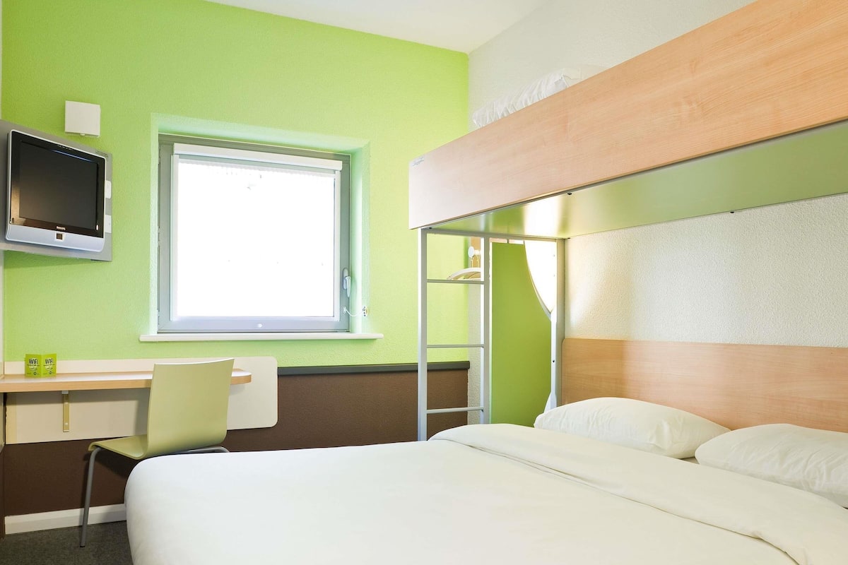 A hotel room with a bed, a desk with a chair, a television, and a window.