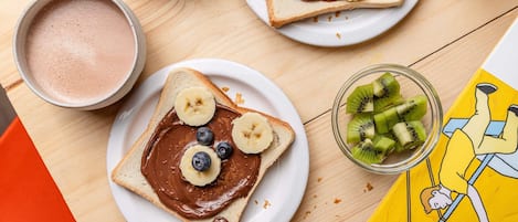 Una mesa de madera con tostadas, crema de chocolate, plátanos, arándanos y kiwi para el desayuno.
