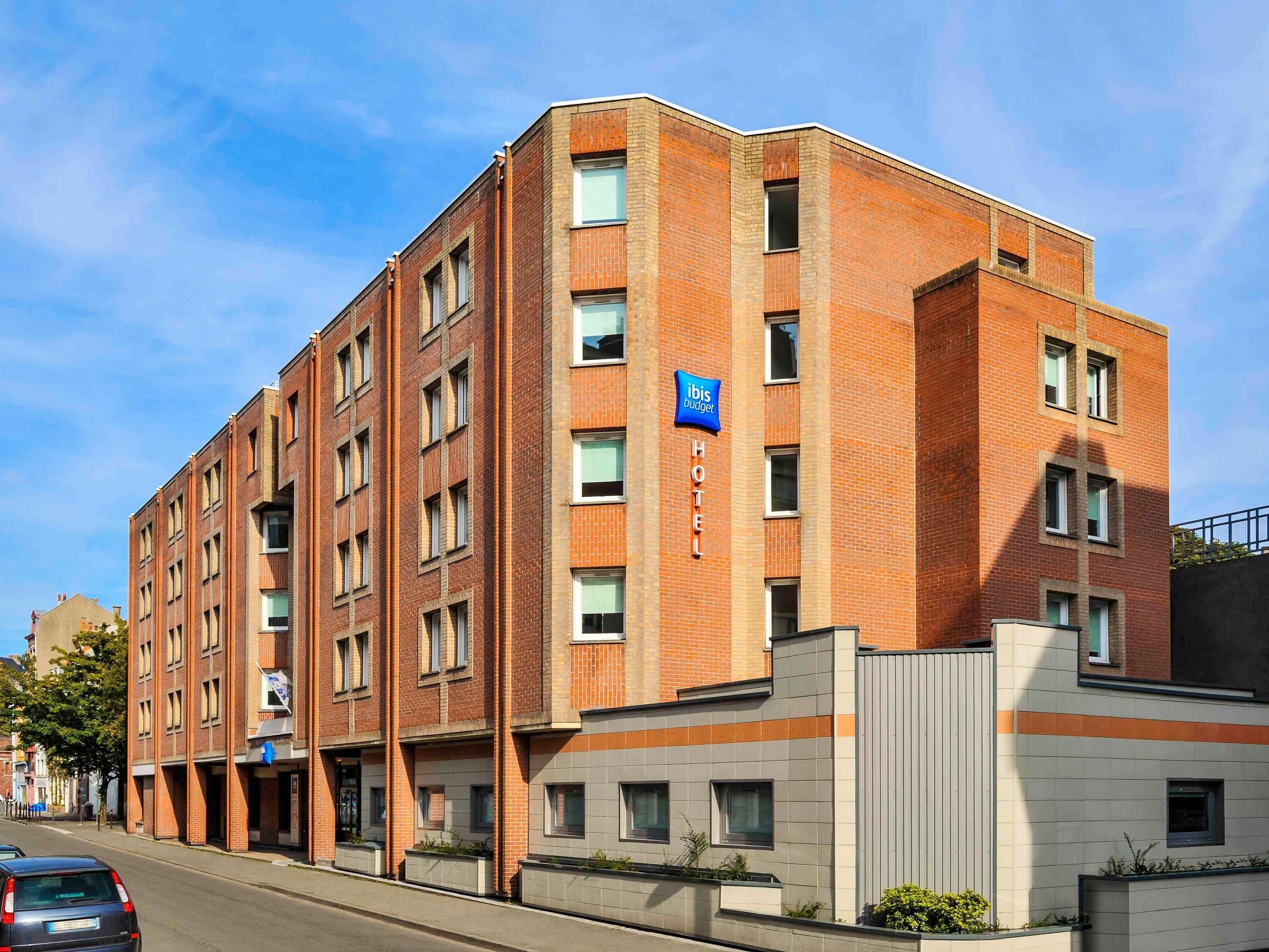 A multi-story hotel with a brick facade, a blue sign indicating it's an ibis budget hotel, and a gated entrance.