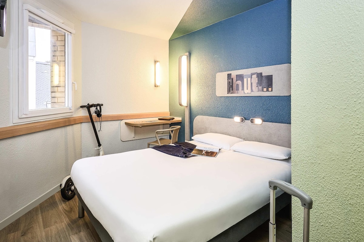 A hotel room with a bed, a desk, a chair, and a window.