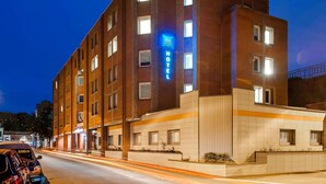 Un hôtel à plusieurs étages, reconnaissable à son grand panneau « Motel », doté d’une façade moderne en briques et de fenêtres illuminées.