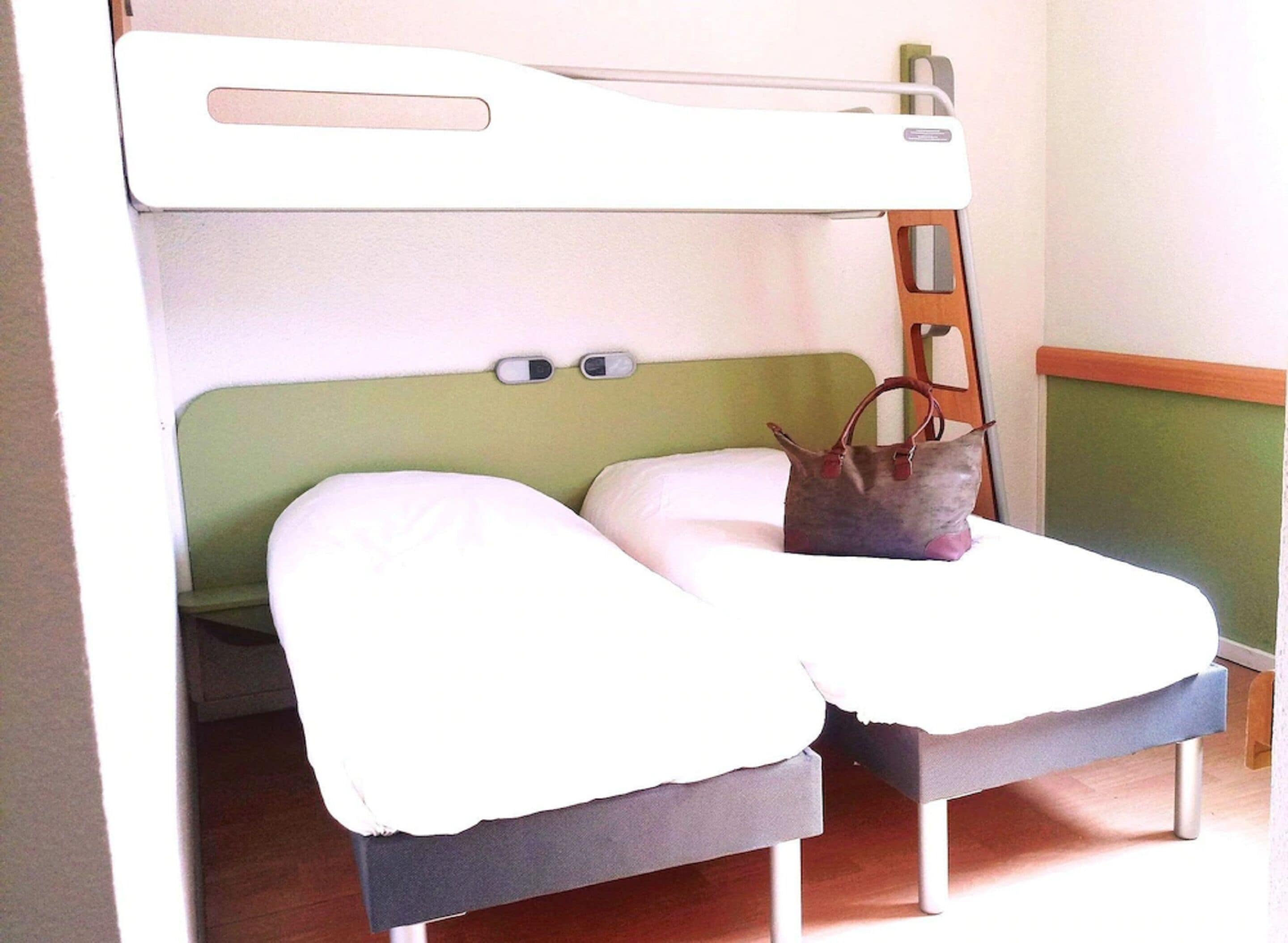 Una cama litera con cabecera verde, dos almohadas y un bolso en la cama inferior.