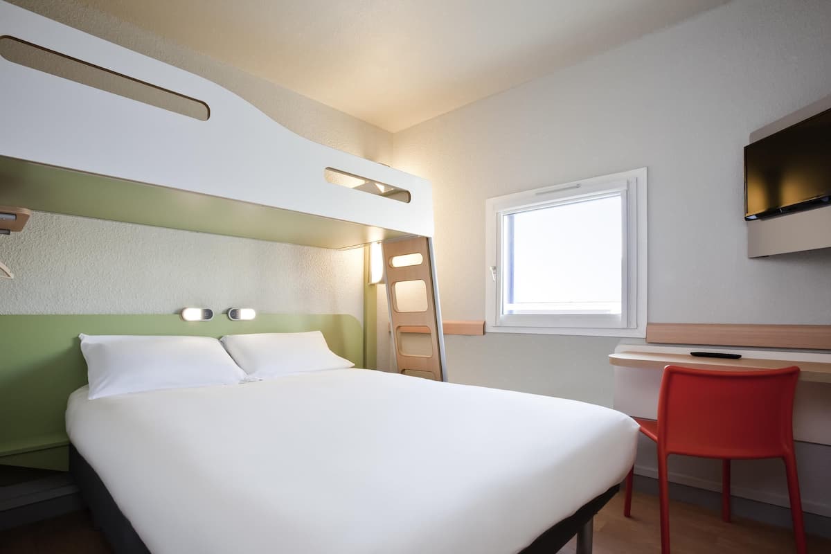 Une chambre d’hôtel avec un lit, un bureau, une chaise, une fenêtre et un téléviseur.