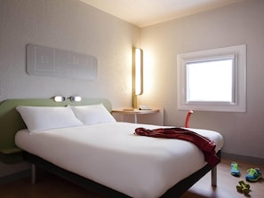 Um quarto com cama, mesa de cabeceira, luminária, janela e uma obra de arte na parede.