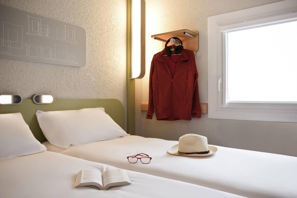 Un lit bien fait, avec des draps blancs, un livre, une paire de lunettes et un chapeau posés sur le lit.