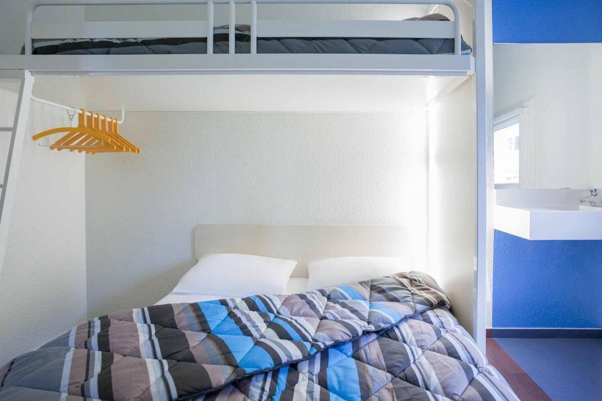 A bunk bed with a white headboard, a hanging yellow hanger, and a striped blanket.