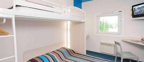 Una cama litera con cubrecama a rayas, un escritorio con silla y una ventana con vista a la vegetación.