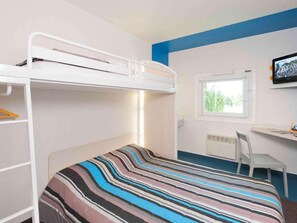 A bunk bed with a striped bedspread, a desk with a chair, and a window with a view of greenery.