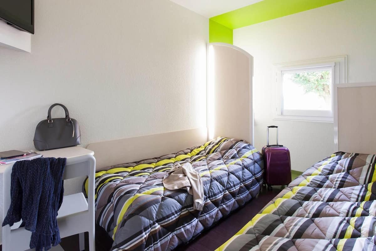 A hotel room with a bed, a desk, a chair, a suitcase, and a window.