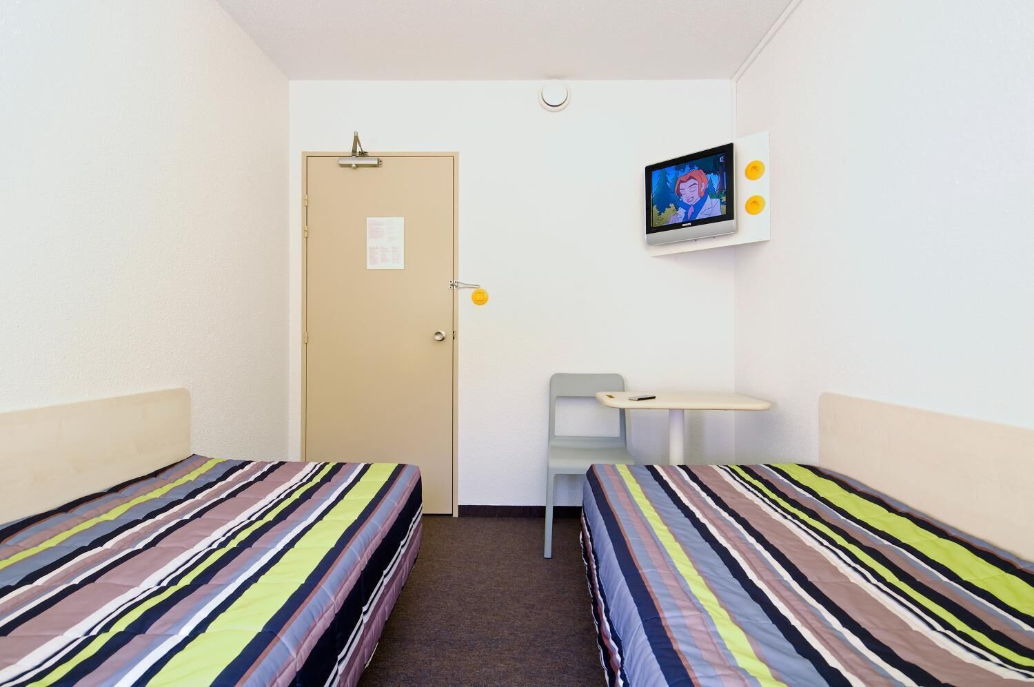 A small, single-room hotel room with two beds, a desk, and a television.