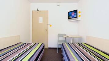A small, single-room hotel room with two beds, a desk, and a television.