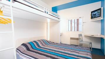 Een slaapkamer met een stapelbed, een beddegoed met strepen, een bureau met stoel, een televisie en een raam met uitzicht op gebouwen.