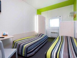 A small, brightly lit room with two beds, a table, and a window.