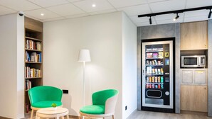 Un interior moderno con una máquina expendedora, una estantería y dos sillones verdes.