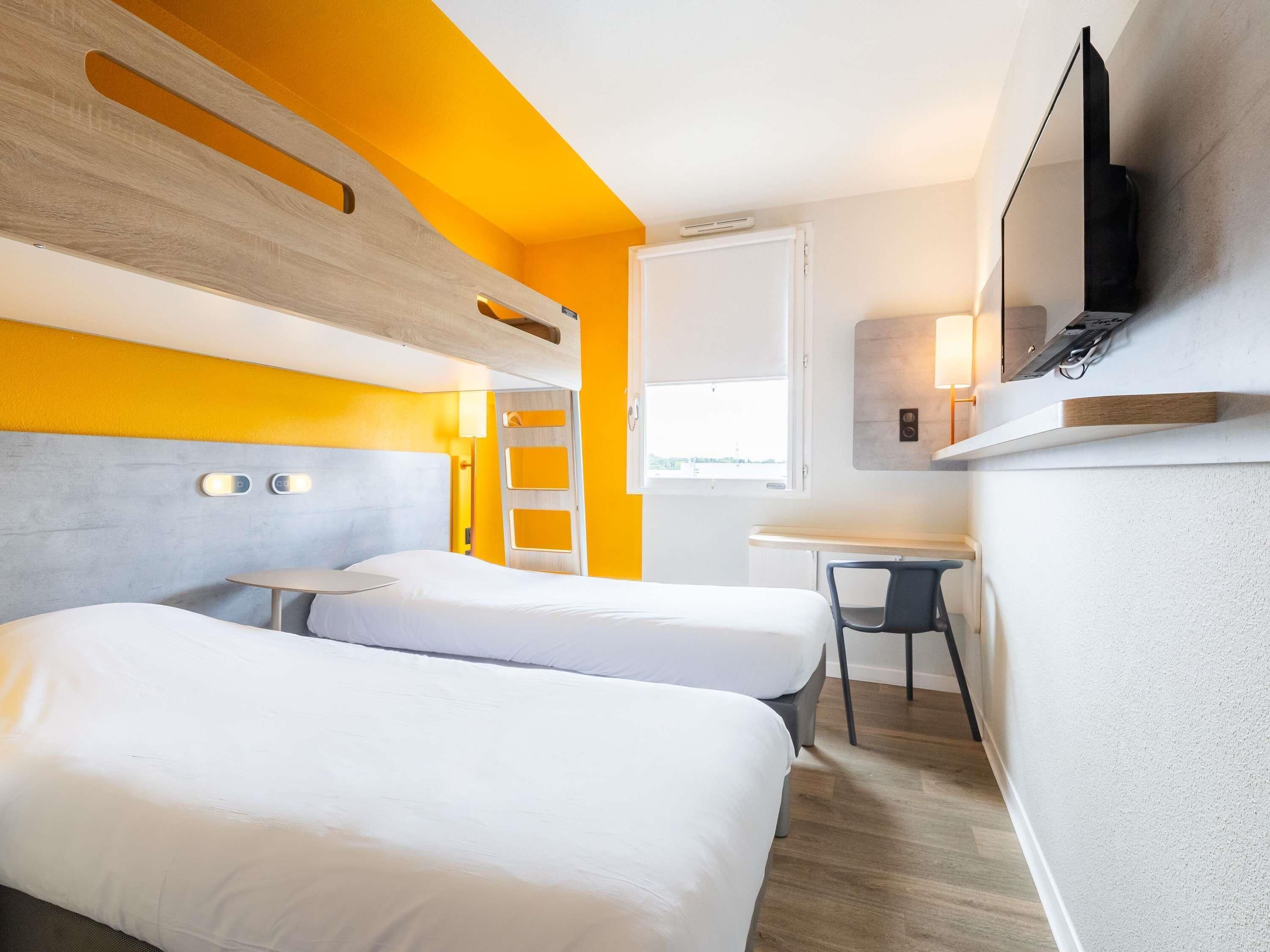 Une chambre d’hôtel moderne équipée de deux lits, d’un bureau, d’une chaise, d’une télévision et d’une fenêtre.