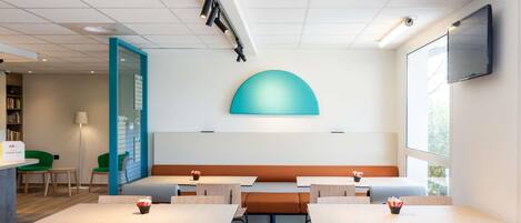 Un comedor moderno con mesas y sillas, una barra con un letrero y una pantalla grande en la pared.