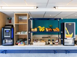 Una estación de desayuno autoservicio con una máquina de café, una vitrina de pan y diferentes condimentos.