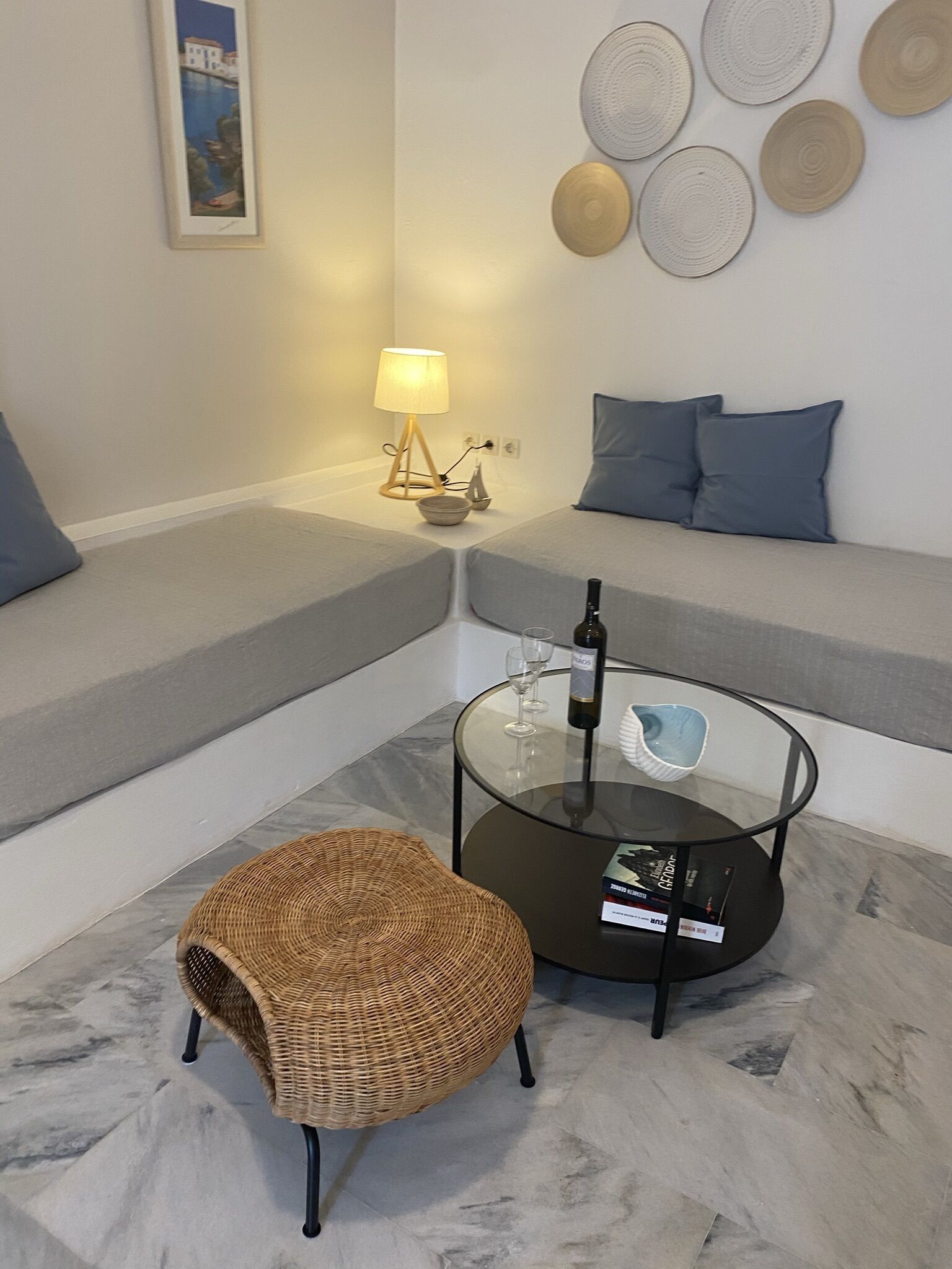 A modern living room with a sofa, a glass coffee table, a wicker chair, a lamp, and decorative plates on the wall.
