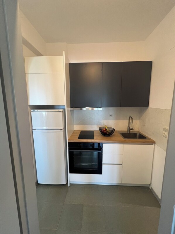 Una cocina compacta con armarios blancos, horno integrado, lavamanos y encimera negra.