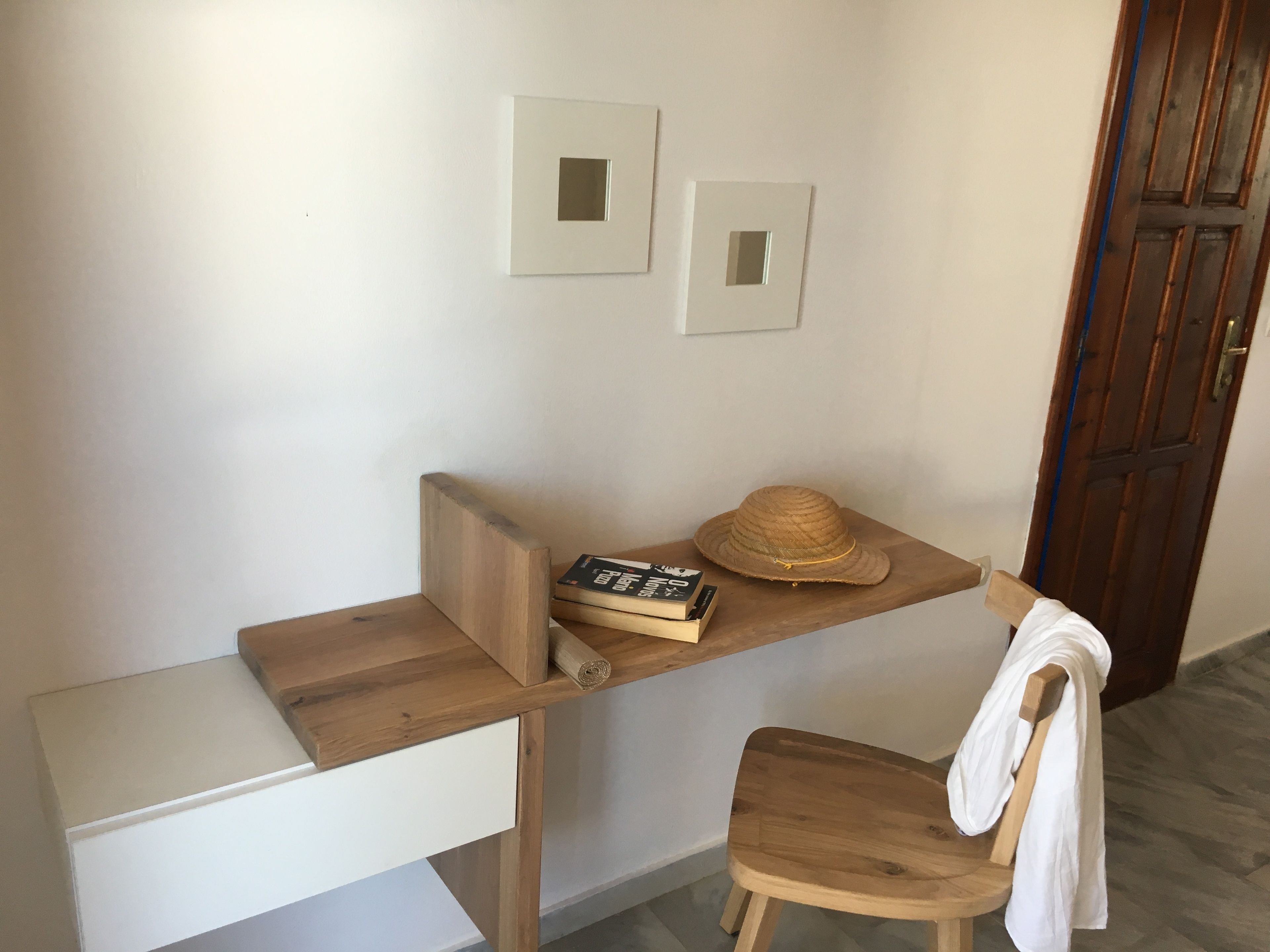 Un petit bureau en bois, avec une chaise blanche, un chapeau et un livre dessus.