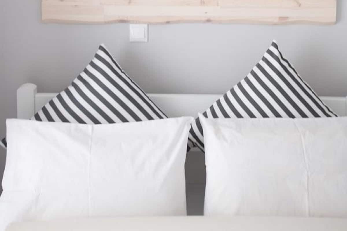 Una habitación con un sofá blanco y dos almohadas a rayas, un cabecero de madera y una pared lisa.