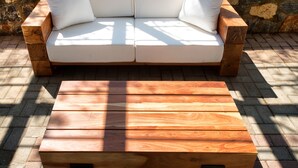 A wooden bench with a cushioned seat in front of a white outdoor sofa with cushions. - Akra Morea Hotel & Residences by GHH (Monemvasia)