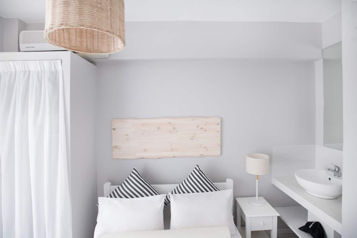 Un baño moderno con un lavabo blanco, un espejo, una mesita de noche con lámpara y una cama con almohadas a rayas.