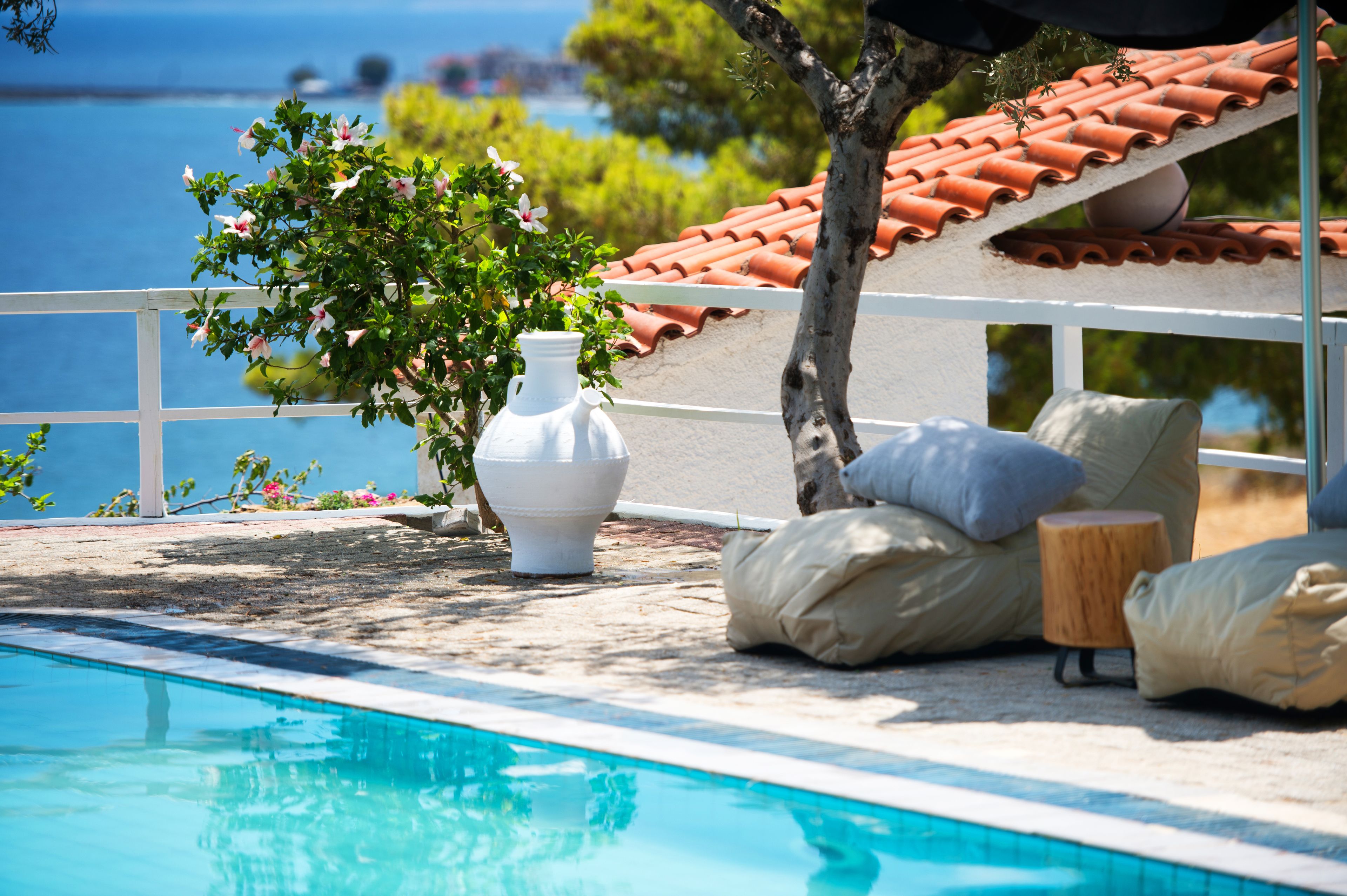 A poolside area with a white vase, beige cushions, and a view of the sea.