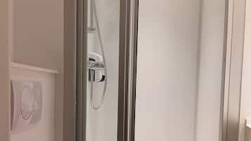 Un baño moderno con ducha envuelta en vidrio, inodoro y panel de control en la pared.