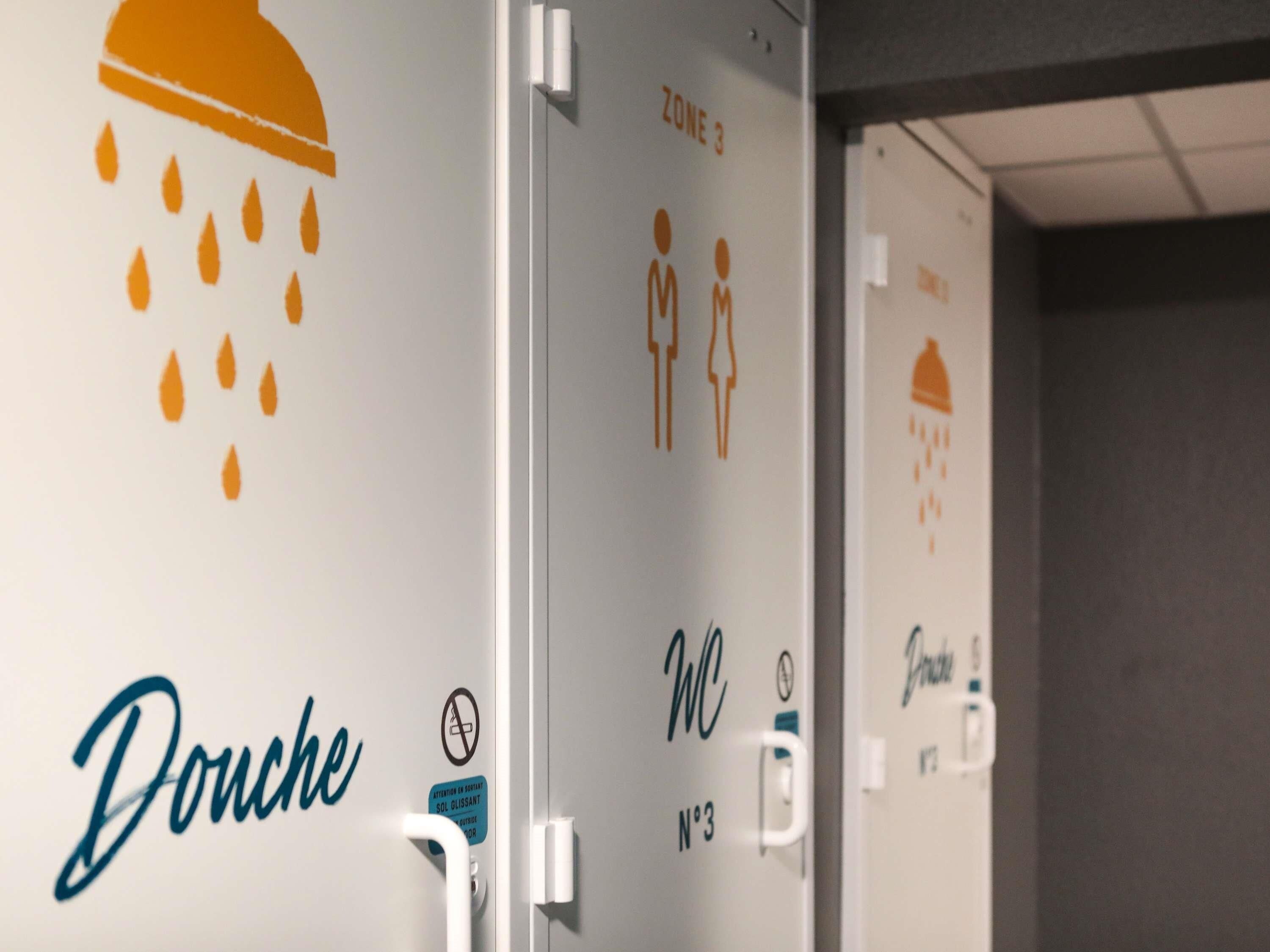 Un lavabans amb assecagats, un senyal de 'Douché', una etiqueta 'Zona 3' i un símbol de 'WC'.