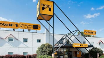 Un hotel con un llamativo letrero 'hotel F1', zona de estar al aire libre y un cielo azul despejado.